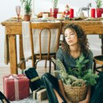 Woman sitting on the floor with depressed facial expression, surrounded by Christmas decor