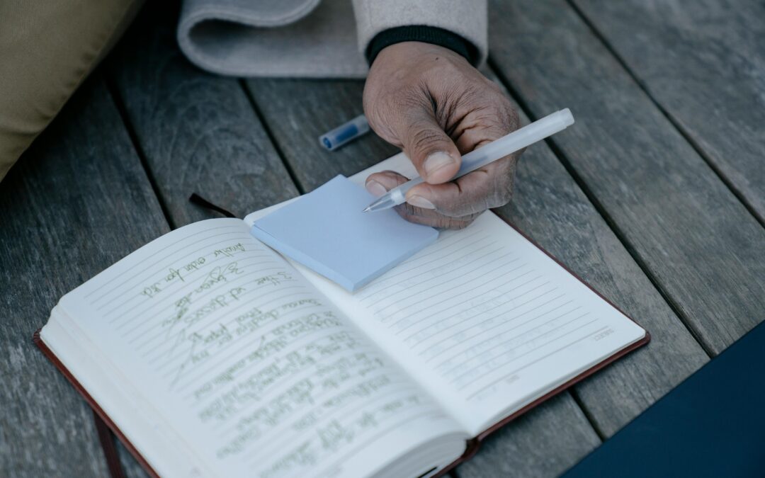 Man sitting on deck, writing on blue sticky notes and journal while making new year's resolutions.