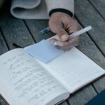 Man sitting on deck, writing on blue sticky notes and journal while making new year's resolutions.